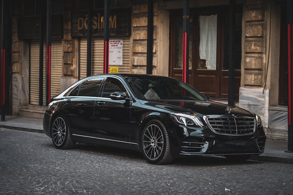 Sleek black luxury sedan parked on a cobblestone street in a historic European city.