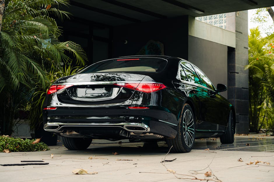 Elegant black luxury car parked outside a modern building amidst lush greenery.